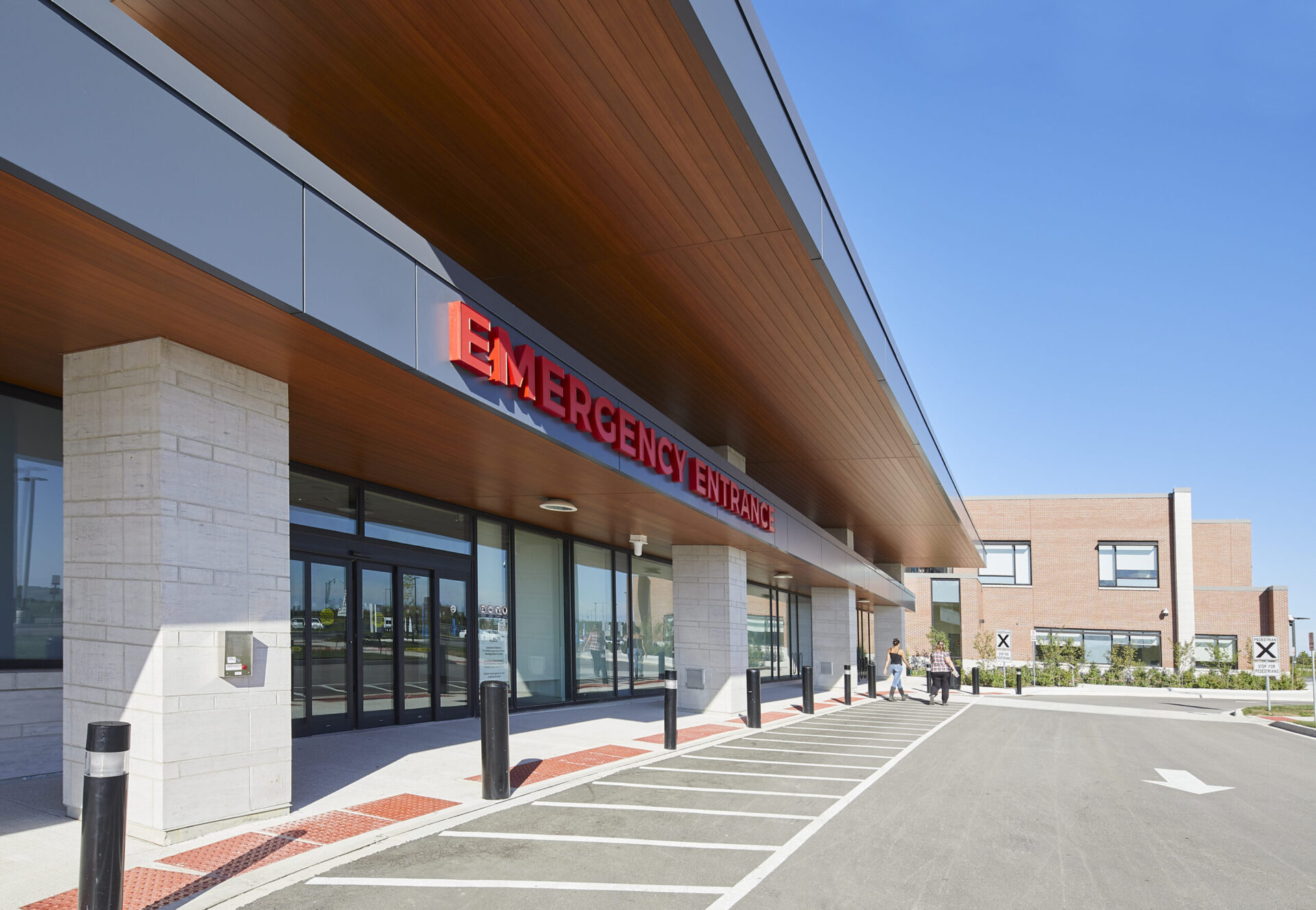 The architecture of a hospital entrance showcases a sign noting the emergency department.