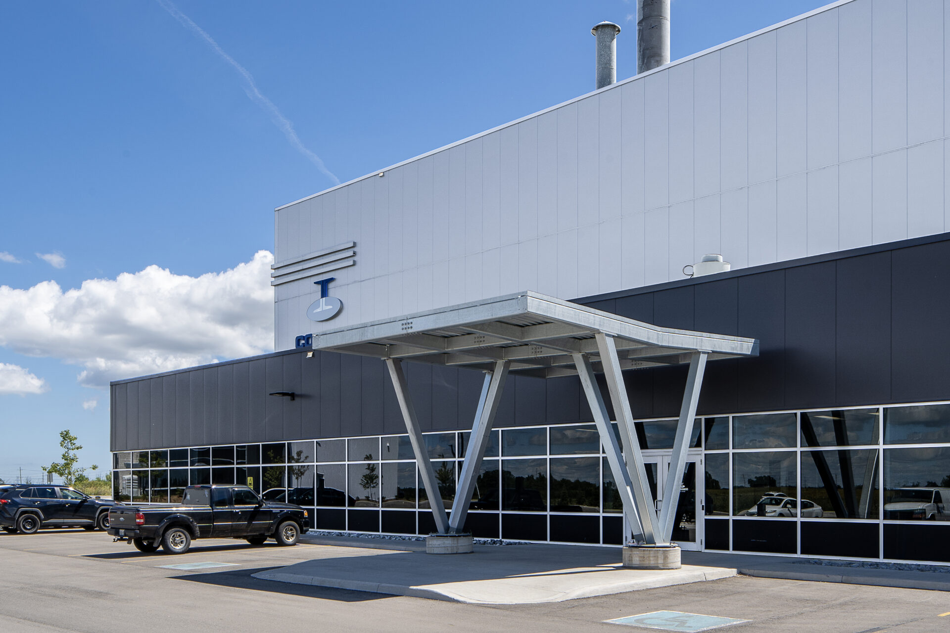 The front of a Steel Galvanizing Plant with cars parked in front of it.