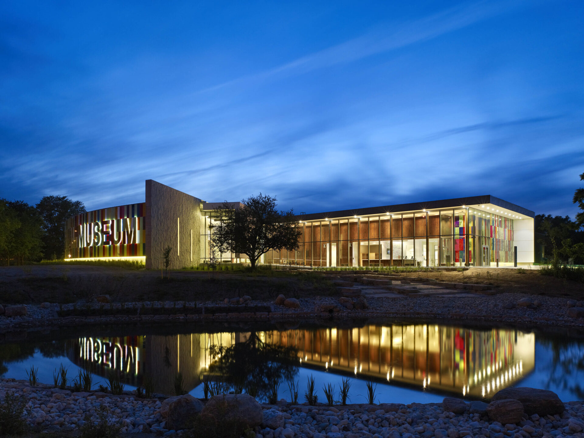 A architecturally-engineered building lit up at night with a reflection in a pond.