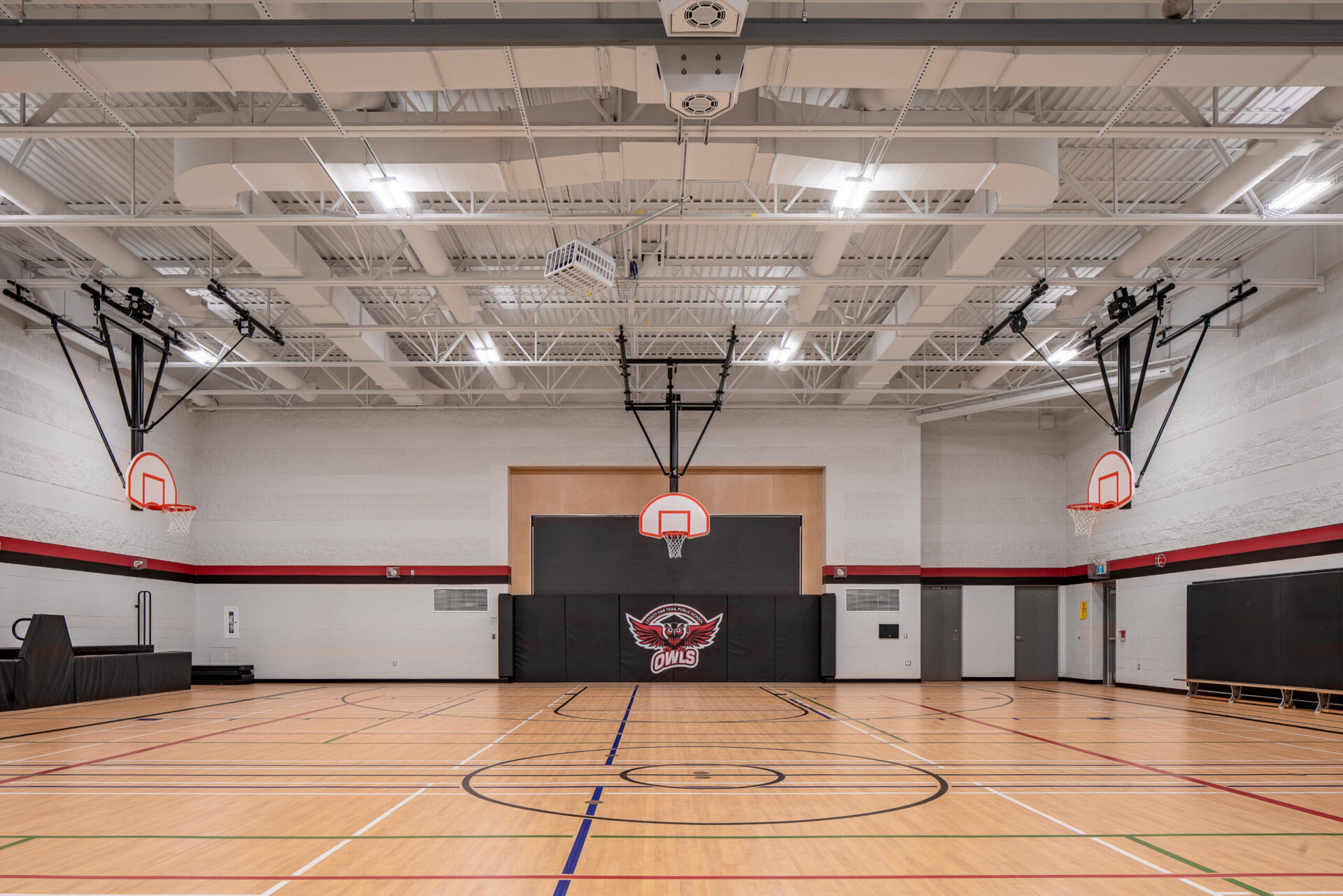 An architecturally designed gymnasium featuring a state-of-the-art basketball court illuminated by modern lighting systems.