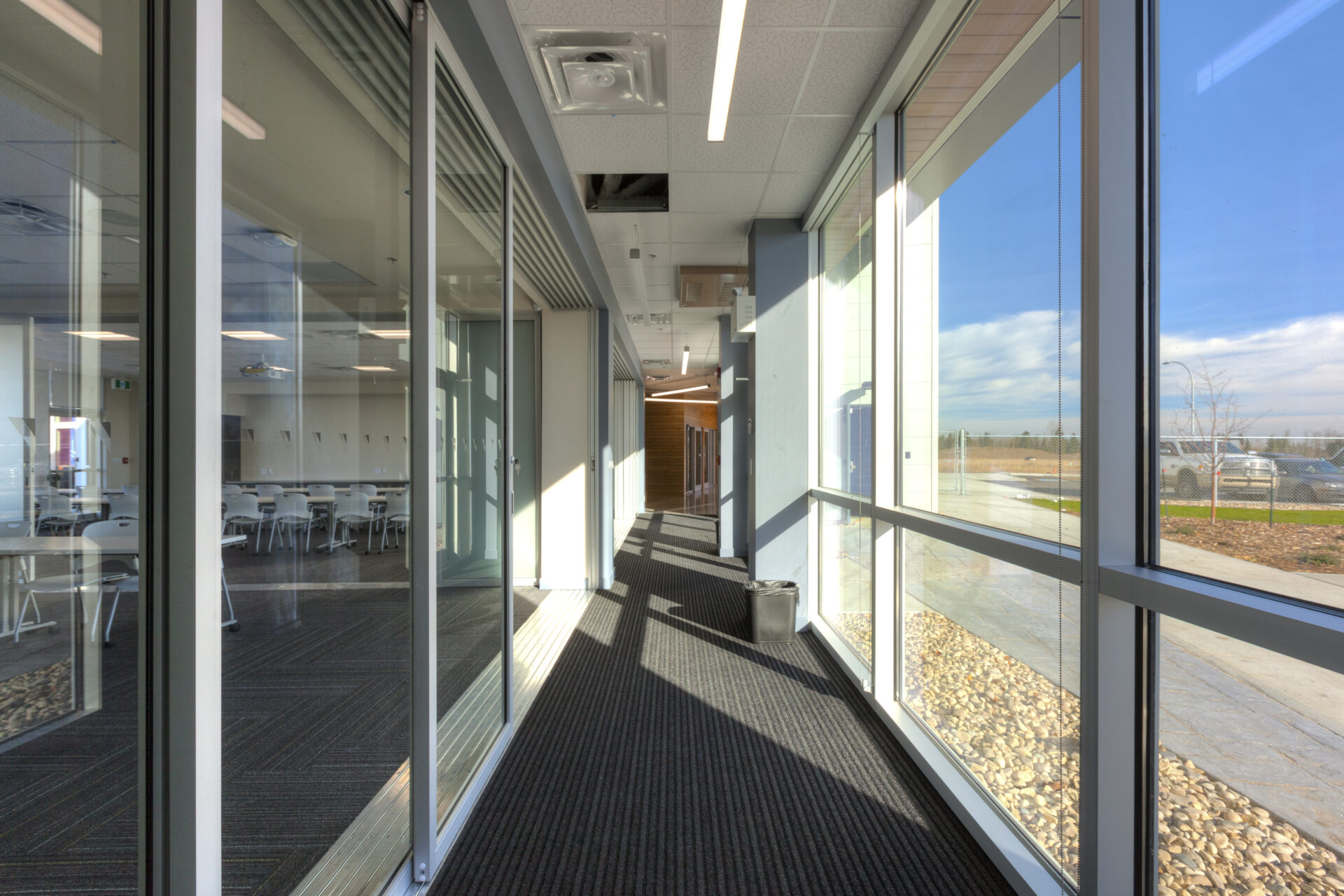 Hallway between large meeting room and outdoor windows. The room is separated by a glass wall to ensure maximum light flows through. The wall is also movable to capture large gathering neds.