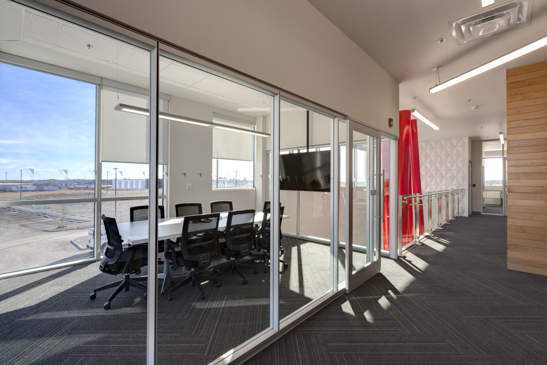 Meeting room enclosed with glass. Window inside of the meeting room is at ground level with outdoors. Meeting room is fitted with a a sleek white table and black chairs.